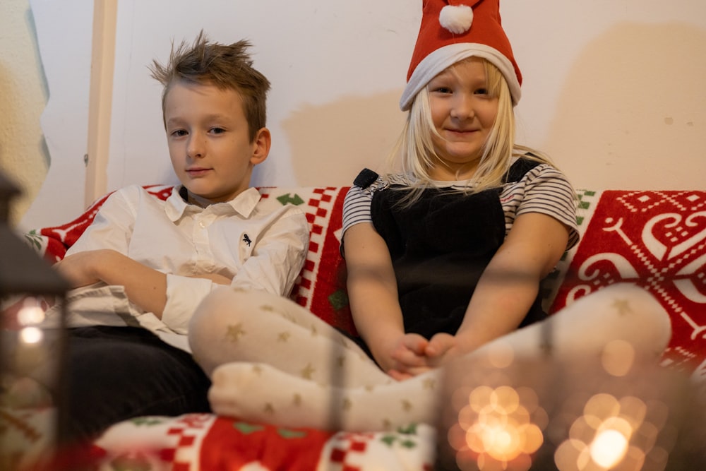 a boy and girl sitting on a couch with a christmas tree