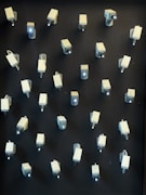 A wall is covered with multiple surveillance cameras arranged in a grid pattern. The cameras are uniform in shape and color, creating a stark and somewhat ominous appearance against the dark background.