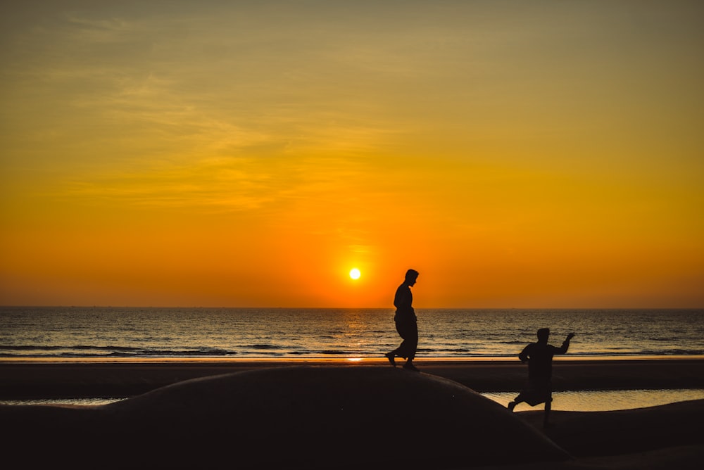 a couple of people walking on a beach at sunset