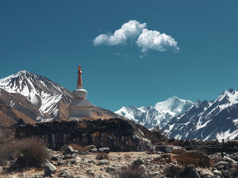 a building with a tower in the middle of a rocky area with snowy mountains in the background