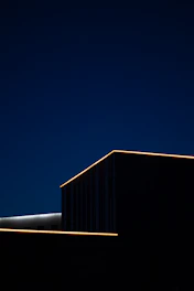 A sleek, modern building silhouette against a deep charcoal sky with subtle gold lighting accents.