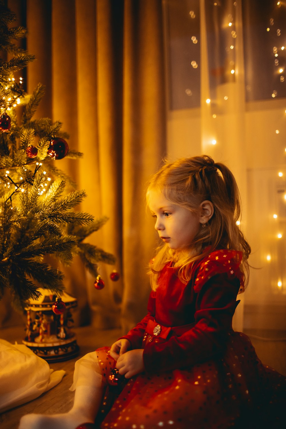 a girl sitting next to a christmas tree