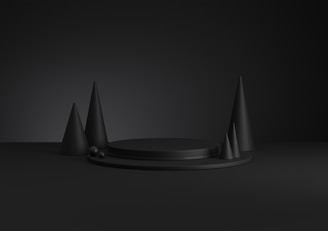 Dark, monochromatic scene with geometrical shapes including cones and a circular platform. The lighting is minimal, casting subtle shadows and creating a dramatic atmosphere.