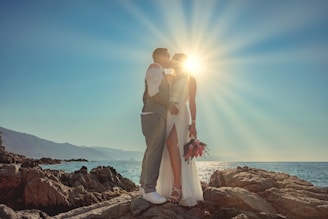 a man and woman kissing on a rocky beach