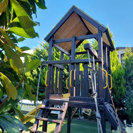 Children playing on a sturdy wooden climbing frame surrounded by green grass.