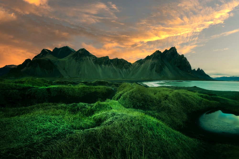 a green landscape with a body of water and mountains in the background