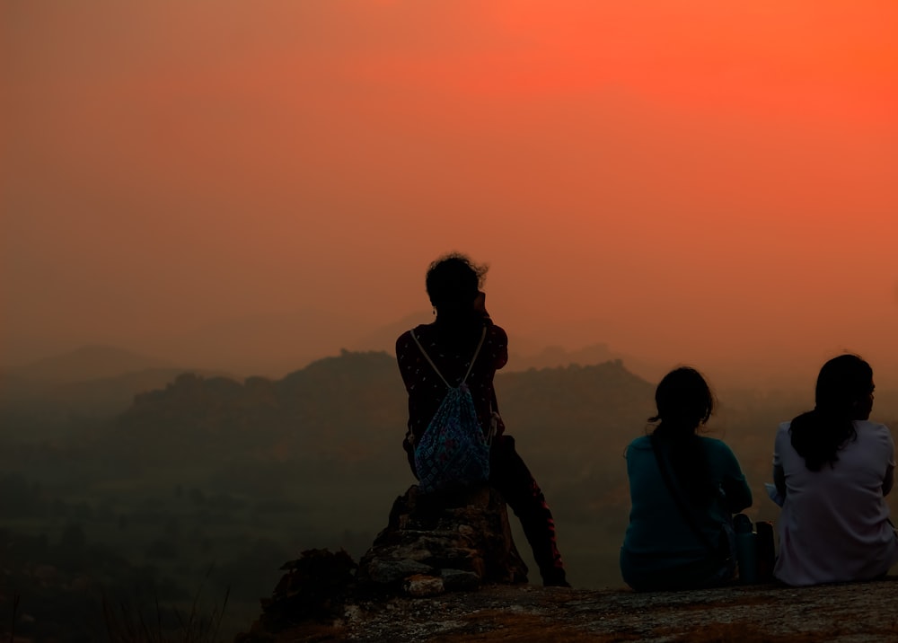 a group of people sitting on a rock looking at the sunset