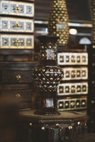 A wooden vase with intricate gold embellishments stands prominently in the foreground. The background features richly detailed wooden drawers with similarly ornate gold accents, creating a luxurious and antique atmosphere.