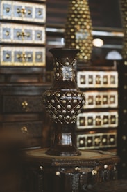 A wooden vase with intricate gold embellishments stands prominently in the foreground. The background features richly detailed wooden drawers with similarly ornate gold accents, creating a luxurious and antique atmosphere.