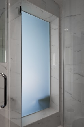 A frosted glass window set within a marble-tiled wall, featuring a chrome handle on the left. The surrounding walls have a polished marble finish with gray veining, adding to the modern aesthetic of the space.