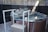 A round, elevated hot tub is surrounded by a border of natural stones. The tub is situated in a fenced backyard area with a gravel ground. White railings provide support for entering or exiting the tub. A small plastic scoop is placed on the edge of the tub.