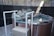 A round, elevated hot tub is surrounded by a border of natural stones. The tub is situated in a fenced backyard area with a gravel ground. White railings provide support for entering or exiting the tub. A small plastic scoop is placed on the edge of the tub.