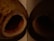 Two dried coconut shells lie on a surface with open hollow centers pointed outward. The lighting is dim, casting deep shadows within the shells and highlighting the textured surface and natural brown color of the coconut husks.