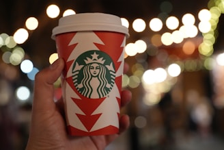 A festive holiday scene with coffee cups and twinkling lights in the background.