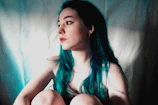 A young person with shimmering teal hair styled in loose waves under soft natural light.