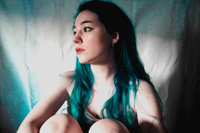 A young person with shimmering teal hair styled in loose waves under soft natural light.