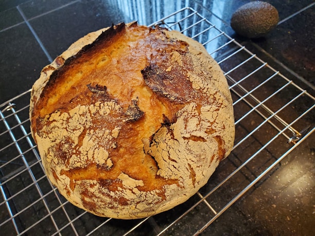 A sunlit wooden countertop with a rustic sourdough loaf cooling on a towel beside vintage measuring cups.