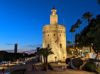a tall stone tower with a clock with Torre del Oro in the background