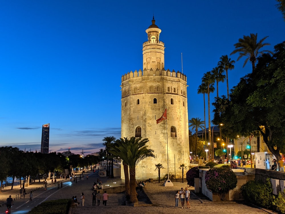 a tall stone tower with a clock with Torre del Oro in the background