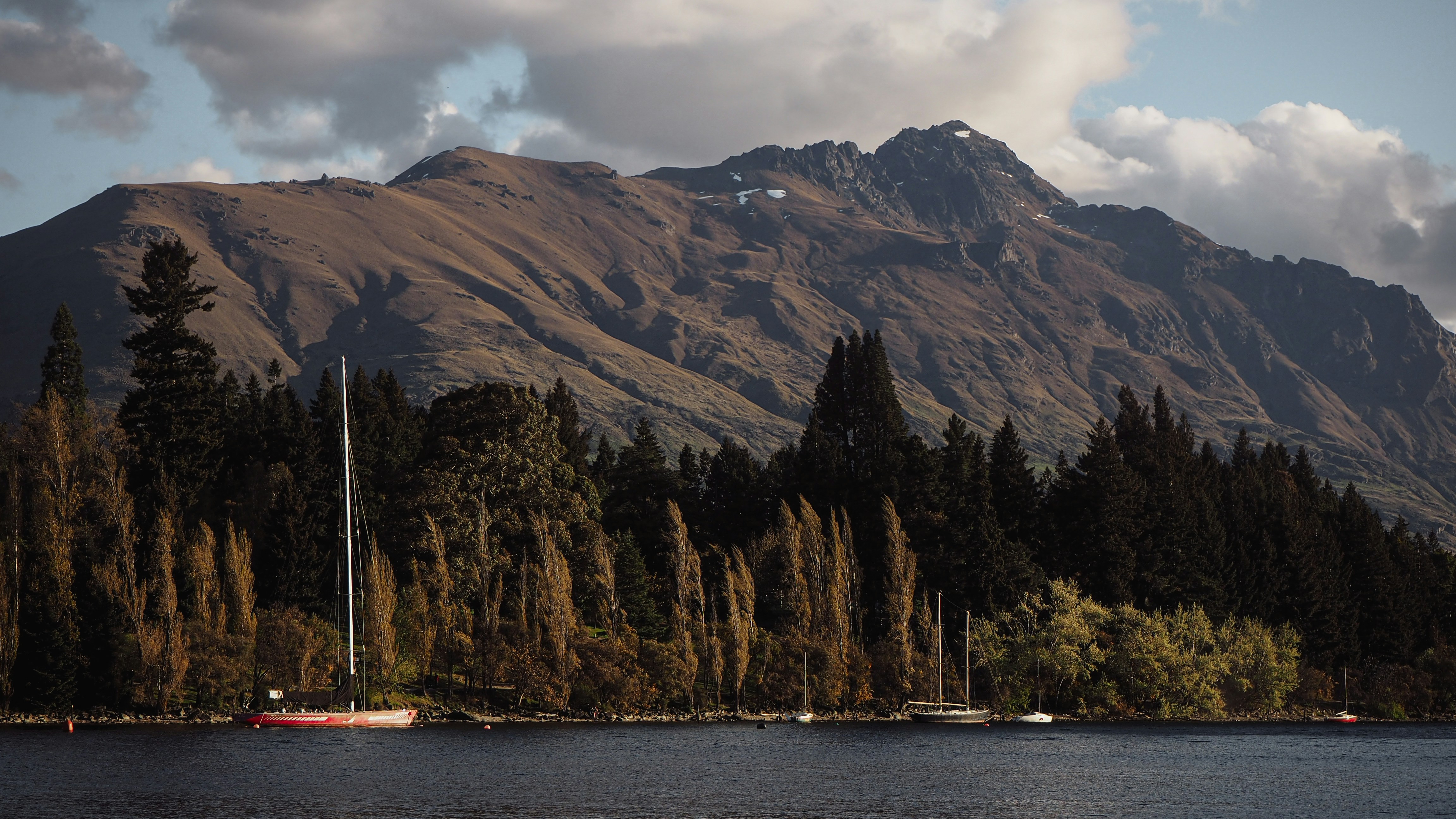 a body of water with boats and trees by it and mountains in the background