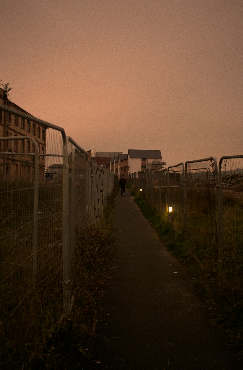 a person walking on a path next to a fence and a building