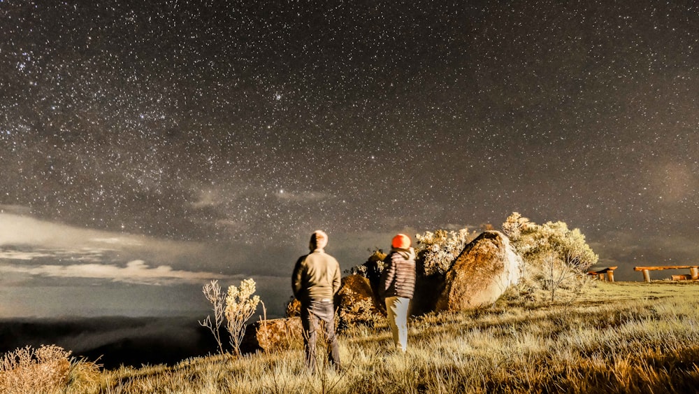 a man and woman standing in a field with hay bales and a starry sky