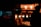A dimly lit street food stall featuring churros under warm, glowing lights. The silhouette of a person is visible next to the stall, creating a contrast with the illuminated food items. Bottles of condiments are also present on the counter.