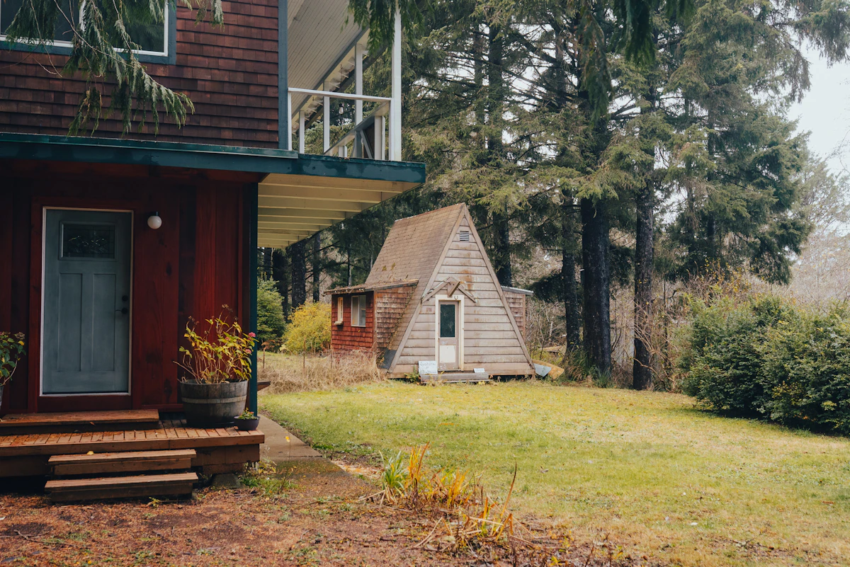 A red house and A-frame cabin among tall trees