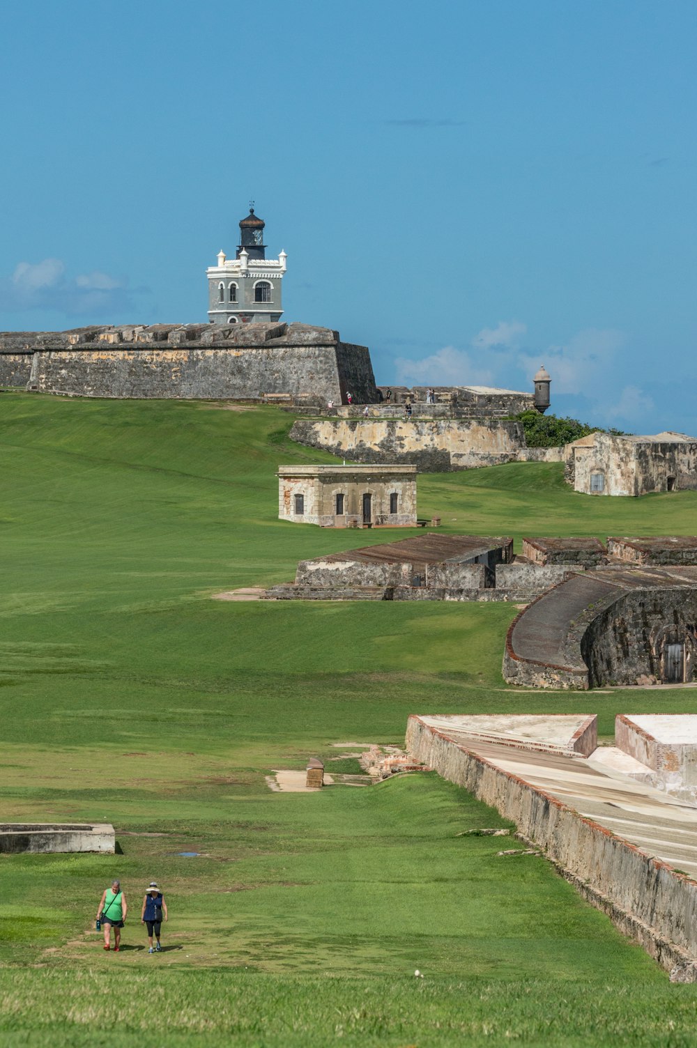 um grupo de pessoas andando em uma colina gramada com um edifício ao fundo