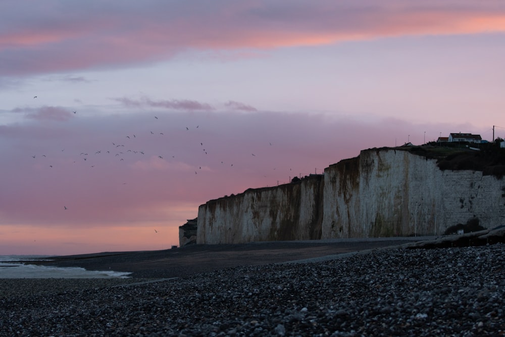 a rocky beach with a cliff and a building on the shore