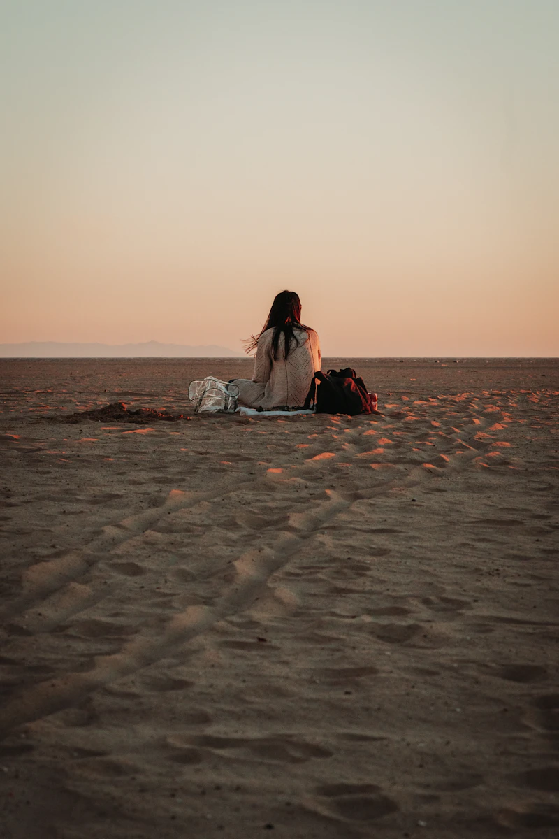 A woman sitting quietly on the sand at sunset