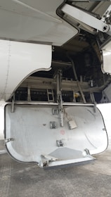 The image depicts the open undercarriage panel of an aircraft, with visible mechanical components and interior structure. The panel shows signs of wear and exposure to dirt, suggesting usage. The background includes parts of the aircraft's wing and various hydraulic and structural elements.