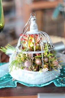 A decorative wire birdcage centerpiece filled with a variety of colorful flowers and greenery, placed on a teal textile with beaded accents.