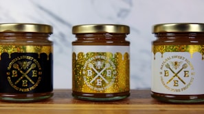 A vibrant display of all three honey varieties—Acacia, Multifloral, and Wild Forest—arranged on a warm honey-colored cloth.