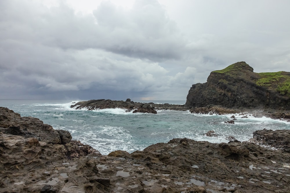 a rocky beach with a large body of water and a cloudy sky