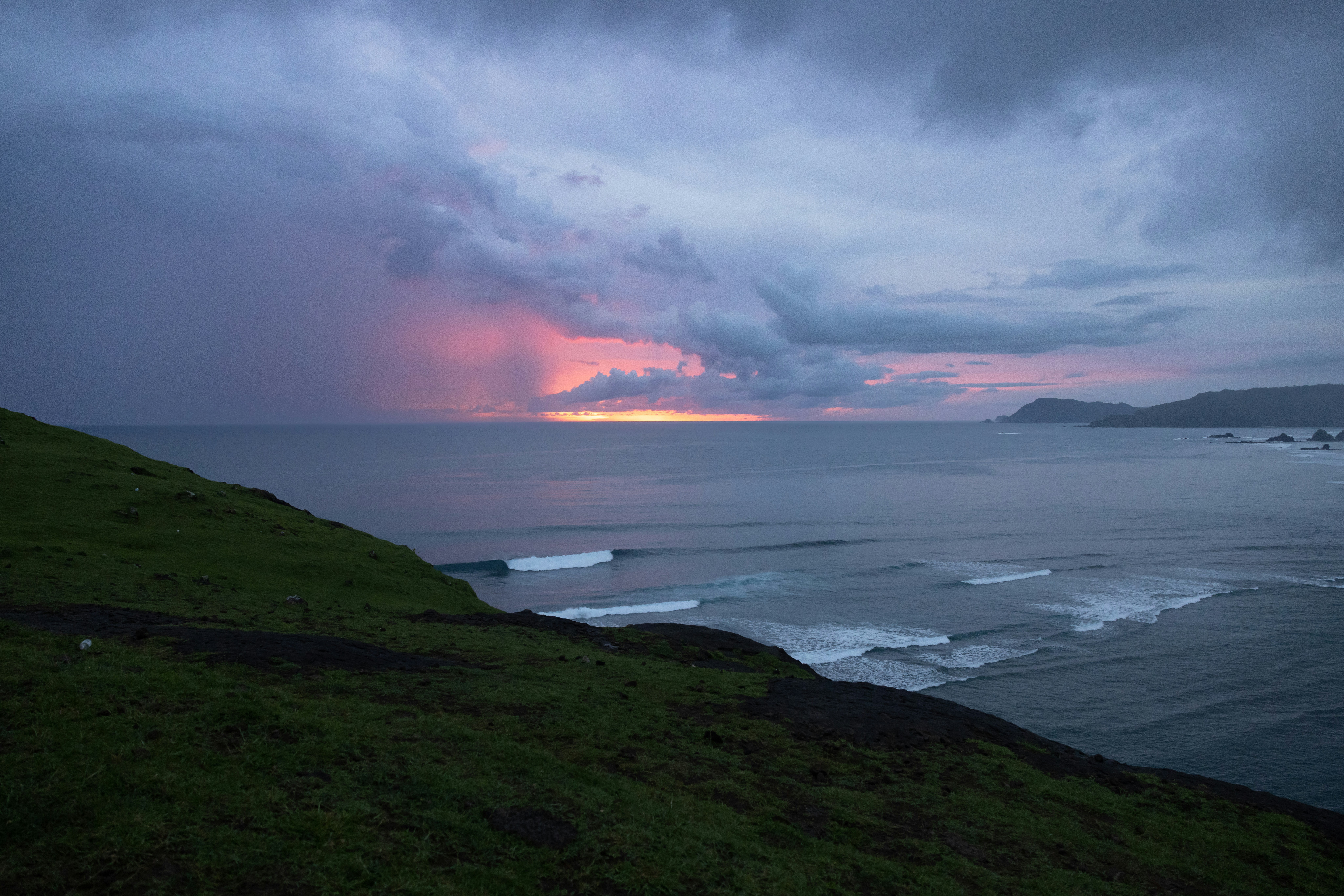a body of water with a land with a hill and a cloudy sky