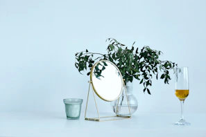 A minimalist vanity setup featuring scented candles, a gold-rimmed mirror, and a small vase with fresh petals