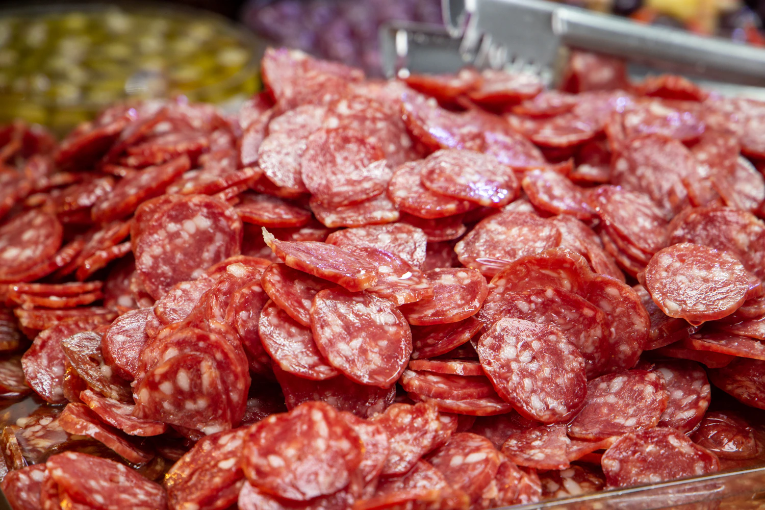 A heap of sliced summer sausage rounds, red with white flecks of fat
