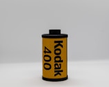 A single roll of Kodak 400 film stands upright against a plain, light gray background. The roll is primarily yellow with bold black text indicating the brand and film speed. The film canister has black caps on the top and bottom.