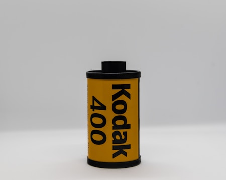 A single roll of Kodak 400 film stands upright against a plain, light gray background. The roll is primarily yellow with bold black text indicating the brand and film speed. The film canister has black caps on the top and bottom.