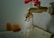 A rusty metal faucet with a red handle is mounted on a wall above a sink. Water is dripping from the faucet, emphasizing a worn or neglected appearance.
