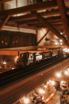 A cozy, elegant display of mini worlds, 3D mechanical puzzles, and DIY miniature houses arranged on a warm wooden table with soft lighting.