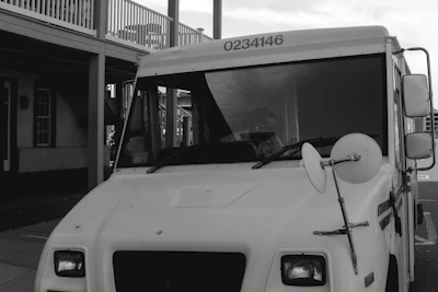 A white box truck with the hibbard deliveries logo parked outside a busy warehouse, ready to load packages.