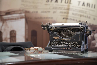 A vintage typewriter on a wooden desk with law books and a pair of reading glasses nearby