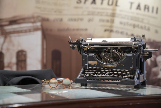 A vintage typewriter on a wooden desk with law books and a pair of reading glasses nearby