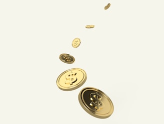 A sequence of golden coins with dollar signs is floating or falling diagonally across a light background. The coins appear shiny and metallic, suggesting wealth or financial growth.