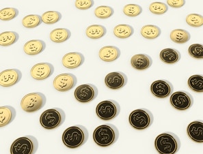 A scattered pattern of gold and dark coins with dollar signs embossed on them, set against a light background.