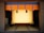 A traditional Japanese room with tatami mat flooring and a wooden frame at the center. The frame is adorned with intricate golden designs at the corners. Above it is a decorative hanging with a blue and orange pattern featuring tassels in black and red.
