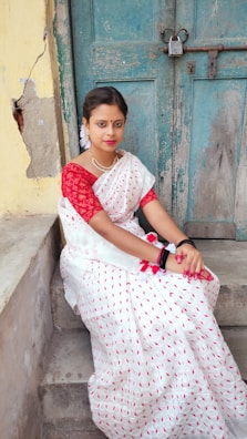 Woman draped in a classic red silk saree standing by an old wooden door.