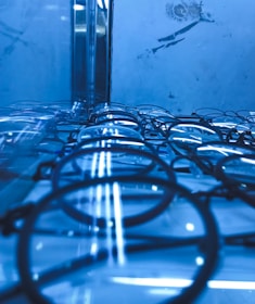 A collection of eyeglasses is neatly arranged on a reflective surface, creating an illusion of infinite repetition. The scene is dominated by a cool blue tone, and the lighting adds a futuristic atmosphere.